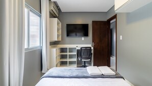 A compact bedroom with a bed, a desk, and a TV. - Apts Near the Beach w/ Full Amenities - RNC (Florianópolis)