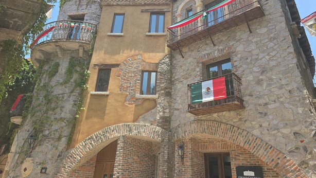 Un edificio histórico con muros de piedra, varios balcones y una bandera.