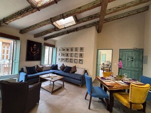 Una sala de estar acogedora con un sofá, sillas, una mesa de centro y una mesa de comedor preparada para dos.