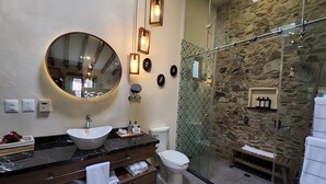 A modern bathroom with a round mirror, a sink, a toilet, and a glass-enclosed shower area.