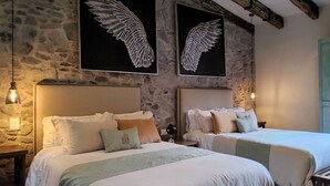 A hotel room with two beds, stone walls, and artwork of wings.