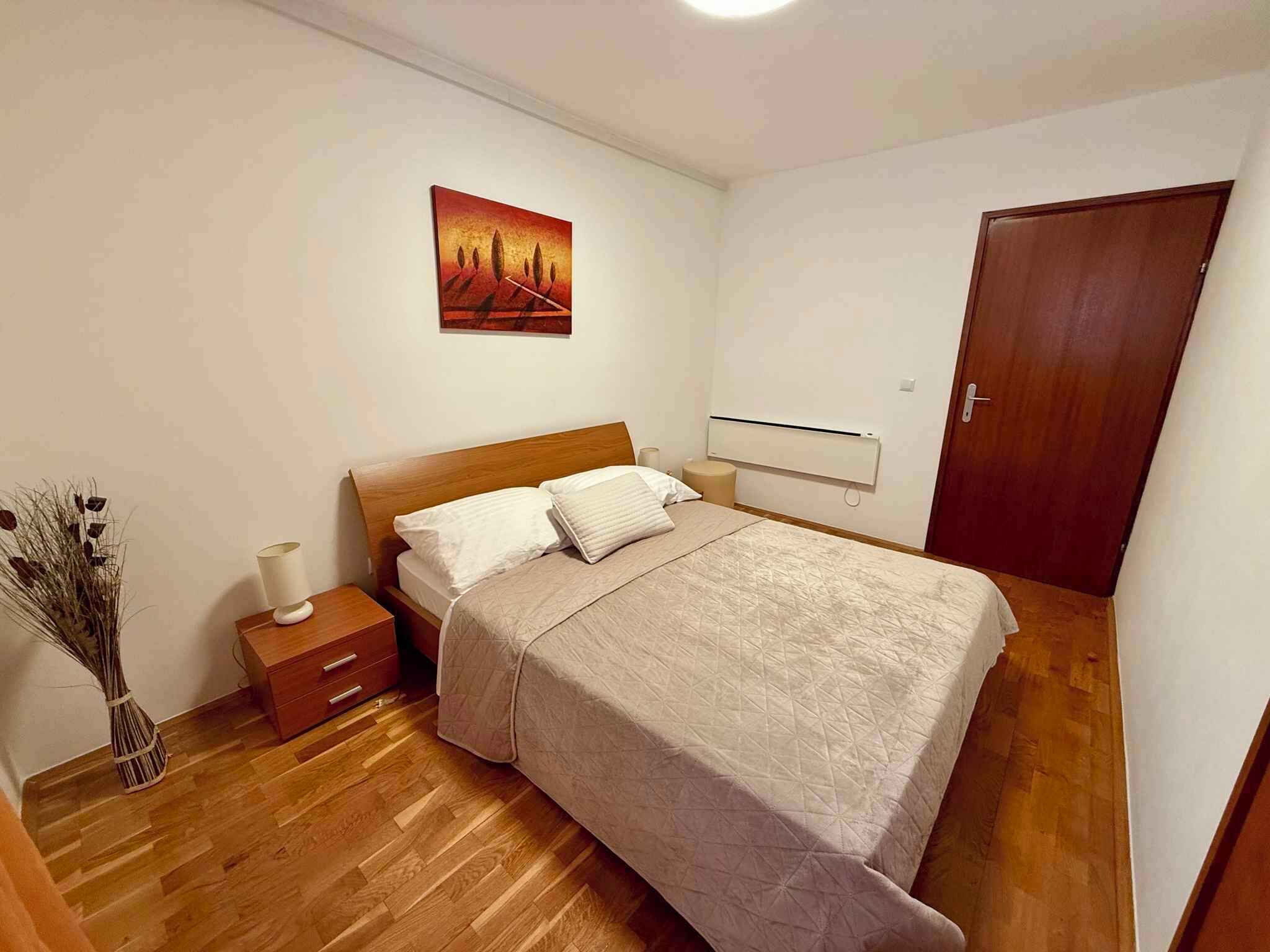 Quarto com cama de madeira, mesa de cabeceira, aquecedor fixado na parede e uma porta.