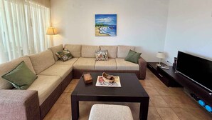 En stue med en beige sofa, et sofabord, et fjernsyn og et maleri på væggen.