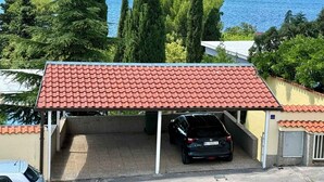 En lukket carport med rødt tag, en parkeret bil og hav og bjerge i baggrunden.