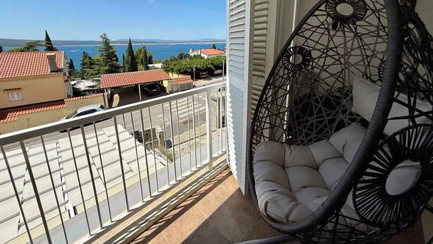 En balkon med hængestol, havudsigt og bygninger i baggrunden.