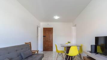 Una sala de estar moderna con un sofá, una mesa de comedor con sillas amarillas y un televisor sobre un mueble.