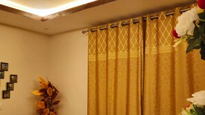 Habitación de hotel con una cama, un sillón amarillo, una mesita con vasos y una cortina de estampado geométrico.
