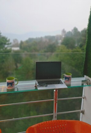 Un portátil sobre una mesa de vidrio, con dos tazas, con vistas a un paisaje verde.