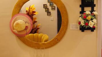 A room with a round mirror, a yellow chair, a bed with a colorful floral bedspread, and a small wooden dresser.
