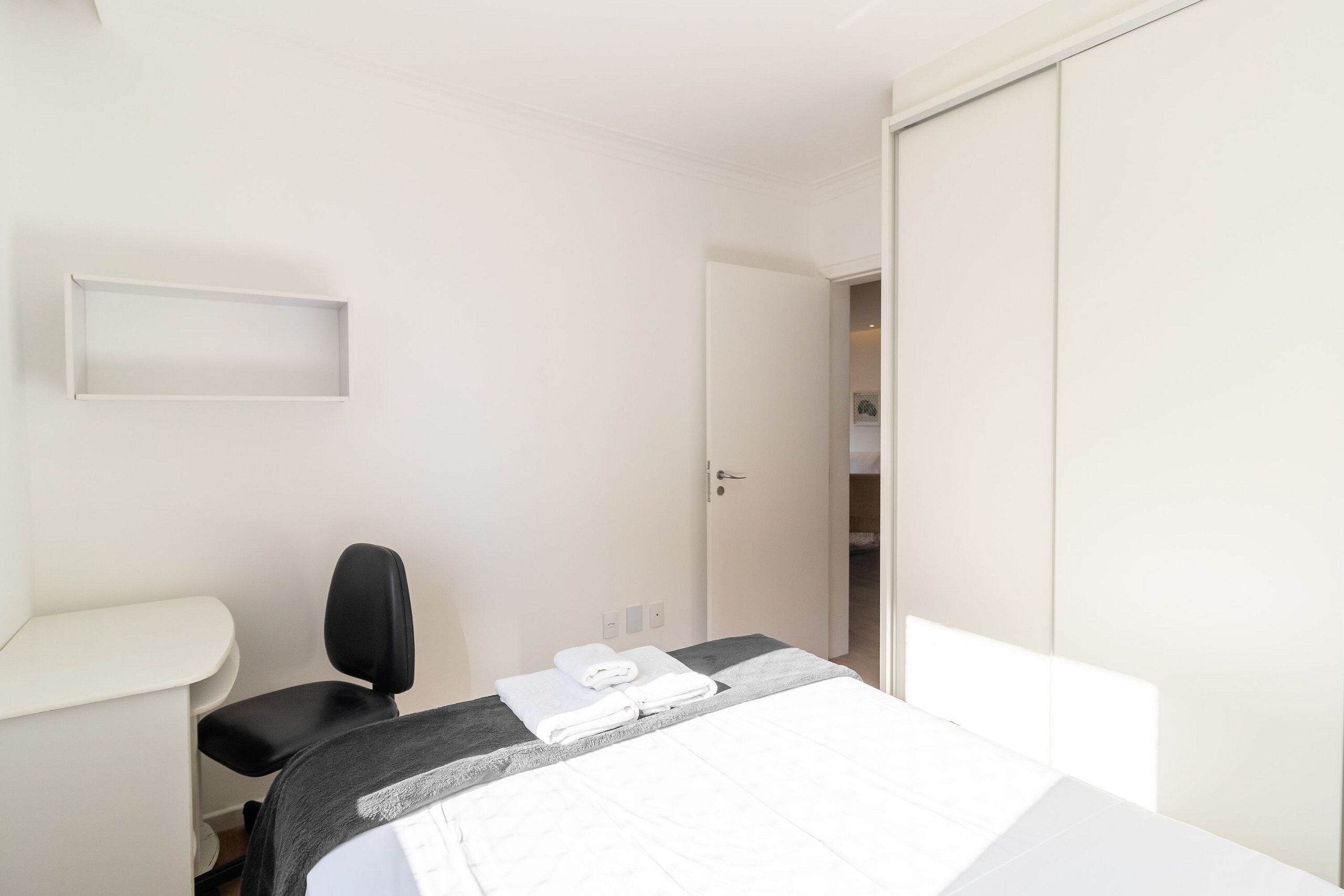 A hotel room with a bed, a desk, a chair, and a wardrobe.