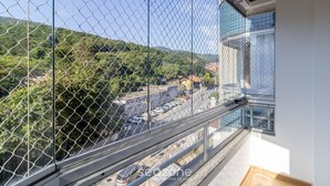 A balcony with a chain-link fence overlooking a hilly landscape and a parking area. - Beautiful 2 Bedroom Apartment in Itacorubi Rlz0301 (Florianópolis)