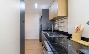 A modern kitchen with a black marble countertop, stainless steel appliances, and wooden cabinets.