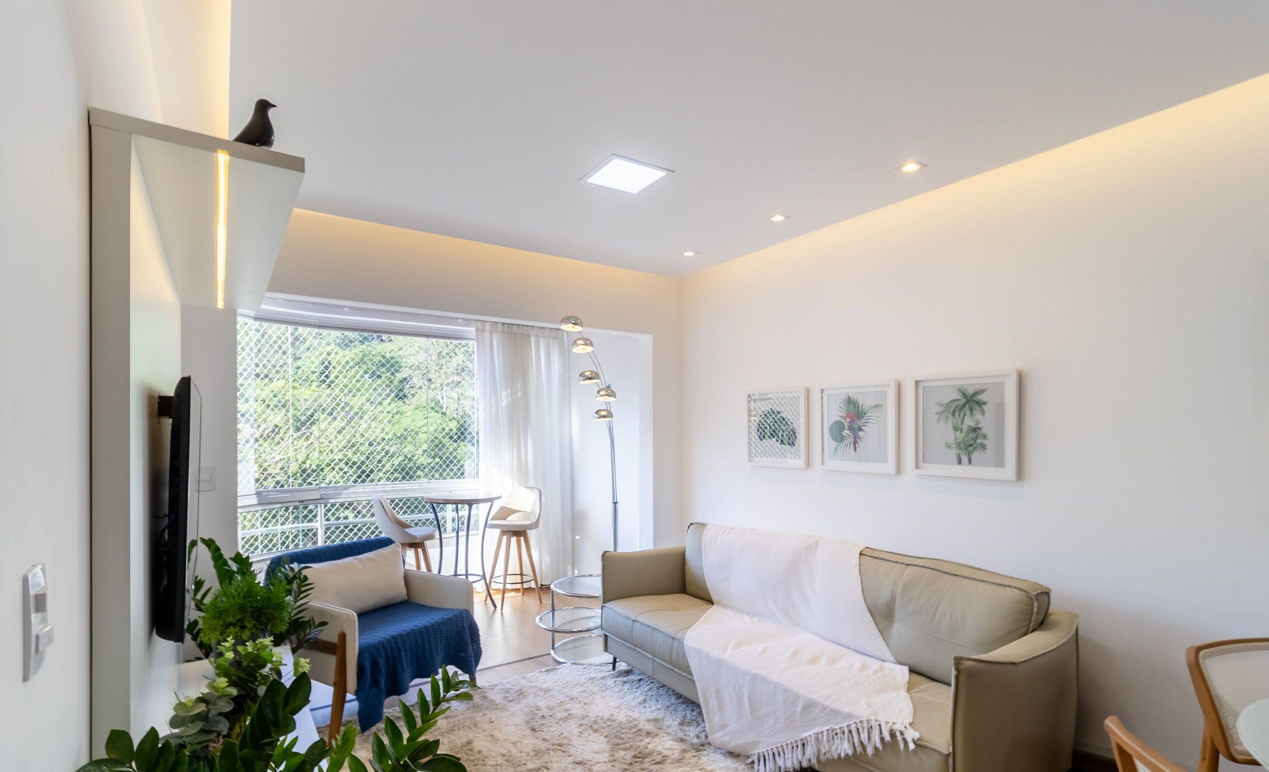 Un salon moderne comprenant un canapé, une table basse et un coin repas avec des chaises. Une grande fenêtre laisse entrer la lumière naturelle et offre une vue sur la verdure environnante.