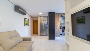 Uma sala de estar moderna com um sofá bege, cozinha ao fundo e um grande pilar preto.