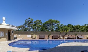 Piscina com espreguiçadeiras e um prédio com chaminé.