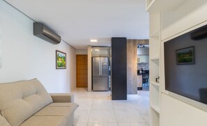 Un salon moderne avec un canapé beige, une cuisine en arrière-plan et une grande colonne noire.