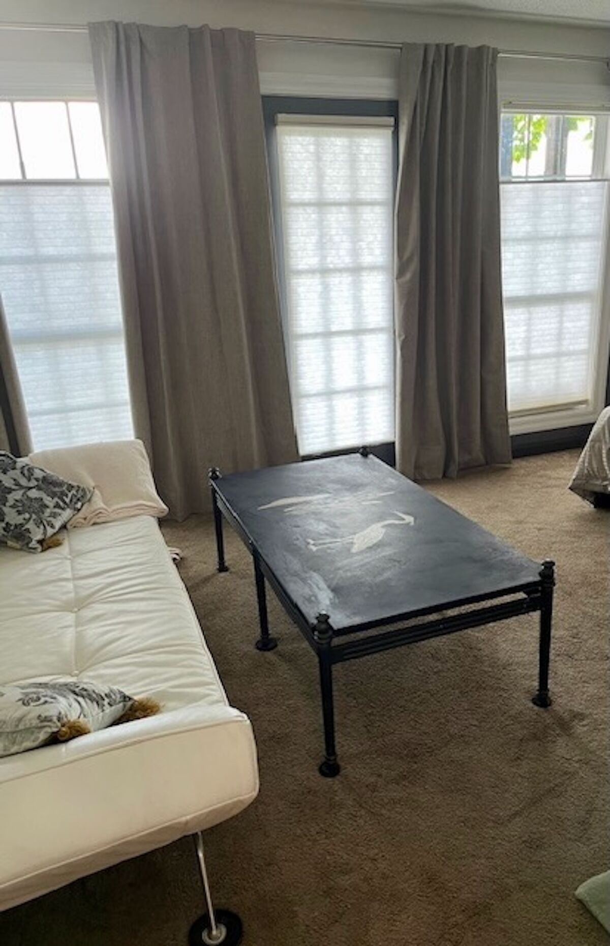 A room with a white sofa, a small table, and large windows with curtains.