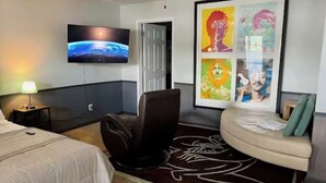 A hotel room with a bed, a reclining chair, a flat-screen TV, and a wall with colorful artwork. - Beautiful 2-bed Garden Lake Apartment, w/ Hot Tub, BBQ, Boat, Parking, Buchanan (Buchanan)