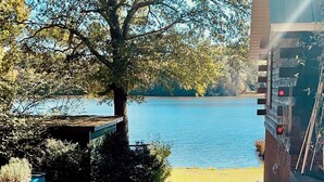 A view of a lake from a building's outdoor area, with a tree and a table with chairs. - Beautiful 2-bed Garden Lake Apartment, w/ Hot Tub, BBQ, Boat, Parking, Buchanan (Buchanan)