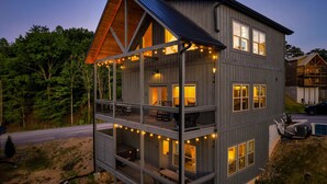 A two-story cabin with a balcony, string lights, and a carport. - NoBunks! 7Beds•Spacious & Near Parkway/Attractions (Pigeon Forge)