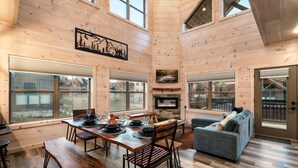 A spacious living area with a fireplace, wooden walls, and large windows. - NoBunks! 7Beds•Spacious & Near Parkway/Attractions (Pigeon Forge)