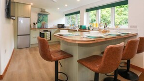 A modern kitchen with a central island, bar stools, a microwave, and a built-in oven. - Cromlech Cottage at Cromlech Manor Farm (Tyn-y-Gongl)