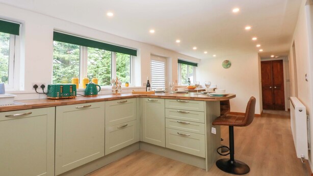 A kitchen with light green cabinets, a wooden countertop, and a bar stool. - Cromlech Cottage at Cromlech Manor Farm (Tyn-y-Gongl)