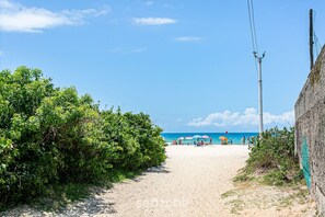 A beach path leading to a sandy beach with umbrellas and people in the distance.