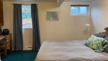 A bedroom with a bed, a desk, a chair, a window with curtains, a map on the wall, and a floor lamp.