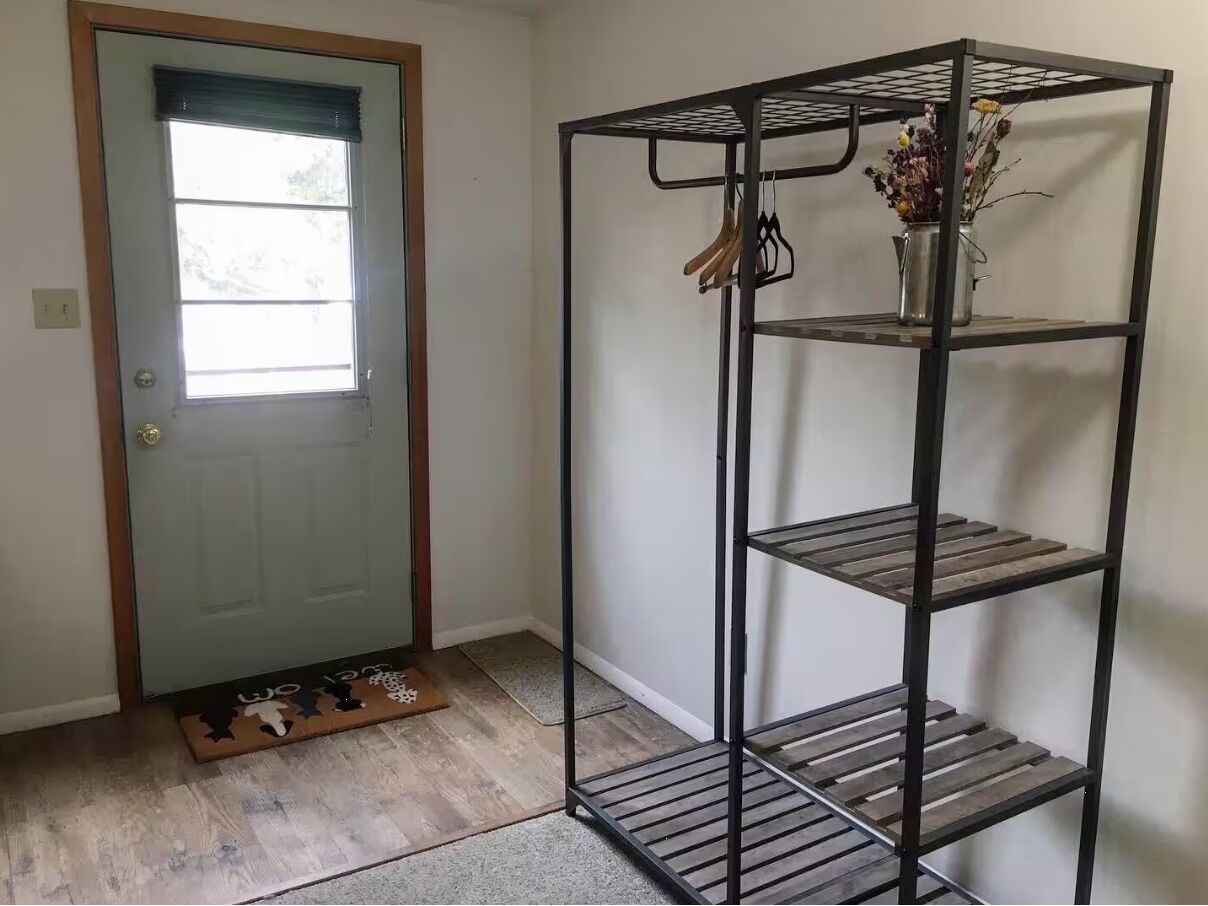Une pièce avec une étagère métallique adossée à un mur, une porte avec une fenêtre et un paillasson.