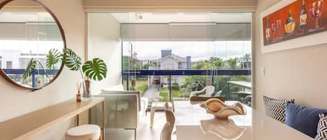 A modern living room with a glass door leading to a balcony, a dining area, and a view of a residential street.