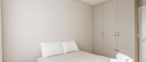 A bedroom with a bed, two pillows, a bedside table, and a wardrobe.