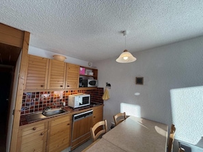 A compact kitchen with wooden cabinets, a microwave, and a sink. There is a dining table with chairs and a pendant light above it. - 2nd floor, terrace, tv, 34m², Les Saisies (Hauteluce)