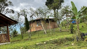 A rustic wooden house with a brick foundation, surrounded by lush greenery and trees. - Casa de Campo CAMVUL lodging; connect with Choco Andean Nature (Gualea)