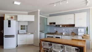 A modern kitchen with white cabinets, a built-in microwave, and a wooden island with bar stools. - Beautiful Seaside Apartment With Barbecue Rig0102 (Florianópolis)