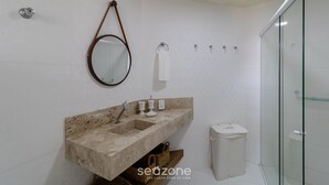 Ein Badezimmer mit Marmorwaschbecken, einem Spiegel, einem Handtuchhalter, einer Duschkabine aus Glas und einem Papierkorb.