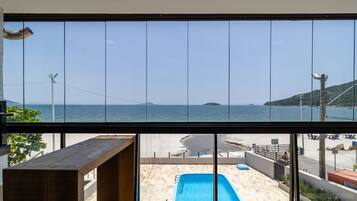 A view from a balcony with a pool, overlooking a beach and the sea.
