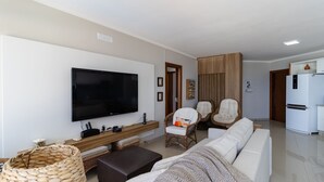 Ein modernes Wohnzimmer mit Flachbildfernseher, einer Couch, zwei Sesseln, einem Holztisch und einem Korbwannenkorb.