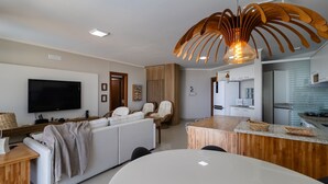 A modern living room with a flat-screen TV, sofa, and a dining area with a round table. - Beautiful Seaside Apartment With Barbecue Rig0102 (Florianópolis)