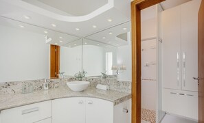Un bagno moderno con uno specchio grande, un lavandino bianco e cabina doccia in vetro.