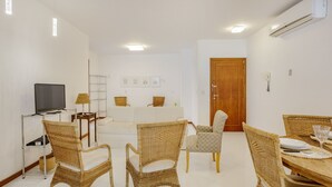 A modern living room with wicker furniture, a flat-screen TV, and a dining area with a table set for two. - Apt one Block sea 260m Praia dos Ingleses Rie0315 (Florianópolis)