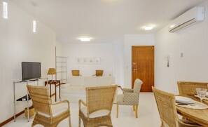 A modern living room with wicker furniture, a flat-screen TV, and a dining area with a table set for two. - Apt one Block sea 260m Praia dos Ingleses Rie0315 (Florianópolis)