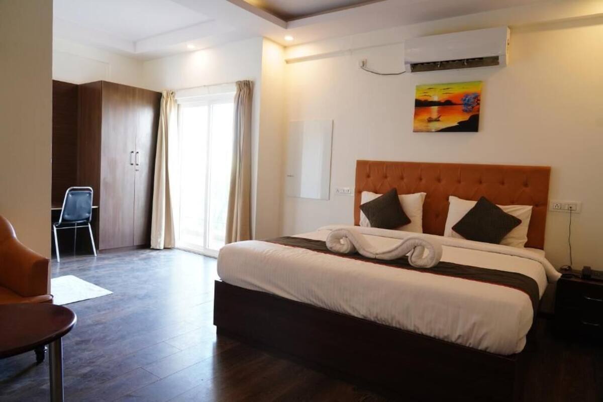 A hotel room with a large bed, a chair, a desk, and a painting on the wall.