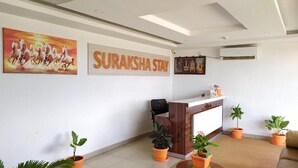 A reception area with a wooden desk, potted plants, and a painting of horses. - Suraksha Stay ITPL Hotel (Bengaluru)