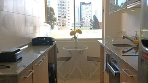 A modern kitchen with a window, a small dining table, and a view of buildings outside.