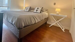 A bedroom with a large bed, a bedside table with a lamp, and a view of the city through the window.