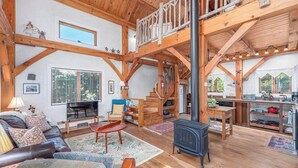 Un vaste espace de vie doté d’un plafond en bois, d’une cheminée, d’une table à manger et d’un escalier menant à un niveau supérieur.
