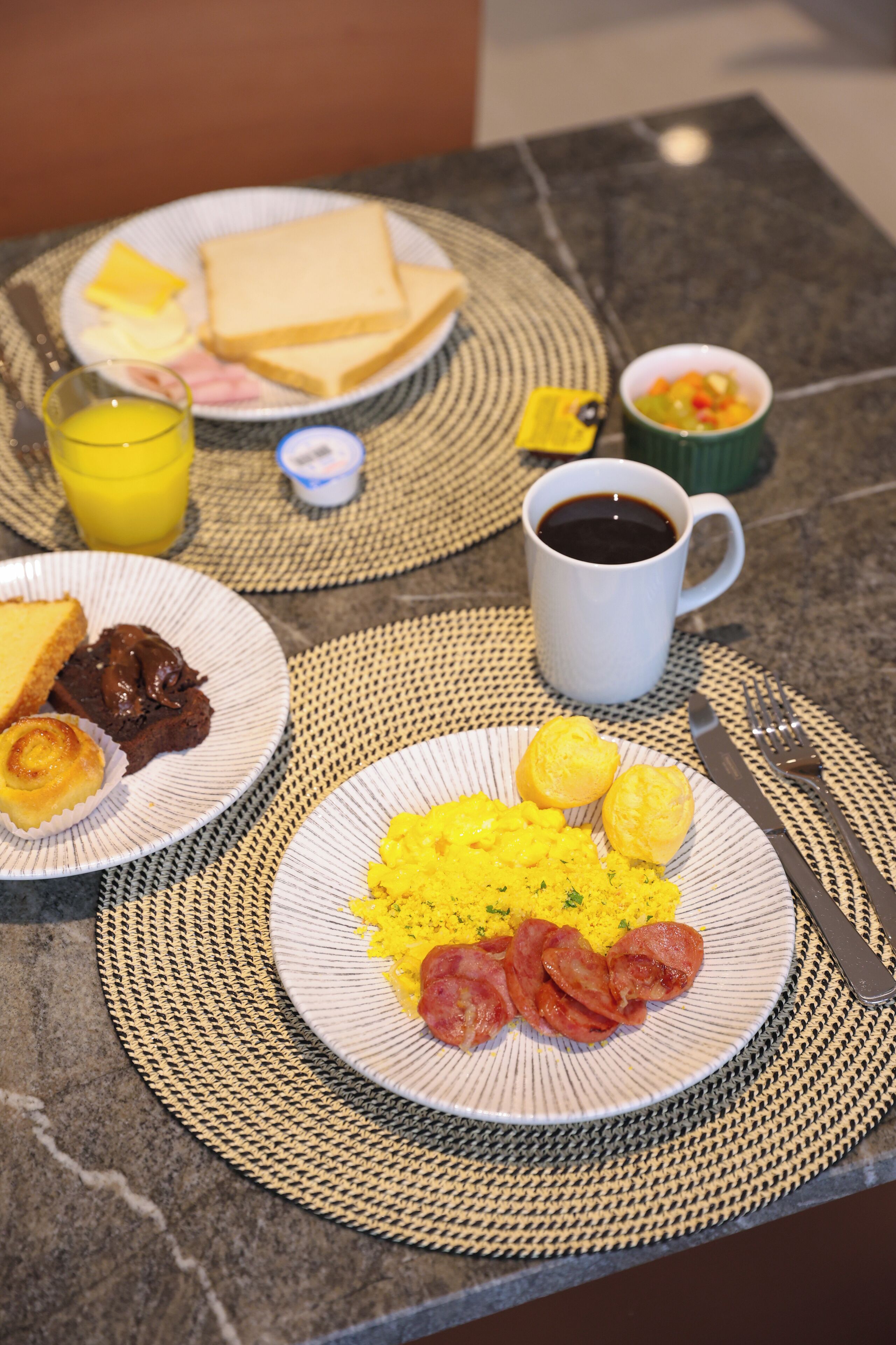Una mesa de desayuno con platos de comida, una taza de café y un vaso de jugo de naranja.
