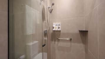 Un box de ducha con paredes de vidrio, un cabezal de ducha de mano, un perchero y un estante con artículos de tocador.
