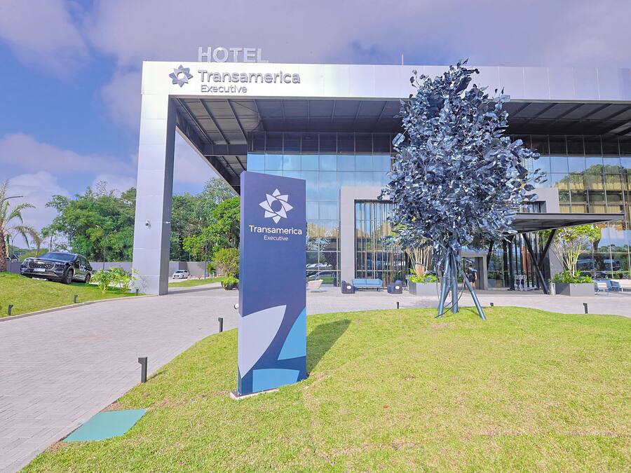 Fachada de hotel moderna de vidrio, una gran escultura metálica y un letrero que indica que el hotel pertenece a la marca Transamerica Executive.